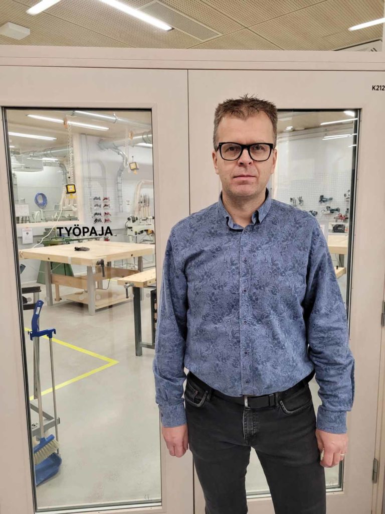 Senior lecturer Antti Hilmola, stands at the front of beige wood workshop in his blue shirt. Bitwards helped create an environment where access control facilitates students to work independently by accessing the machines in the lab. 